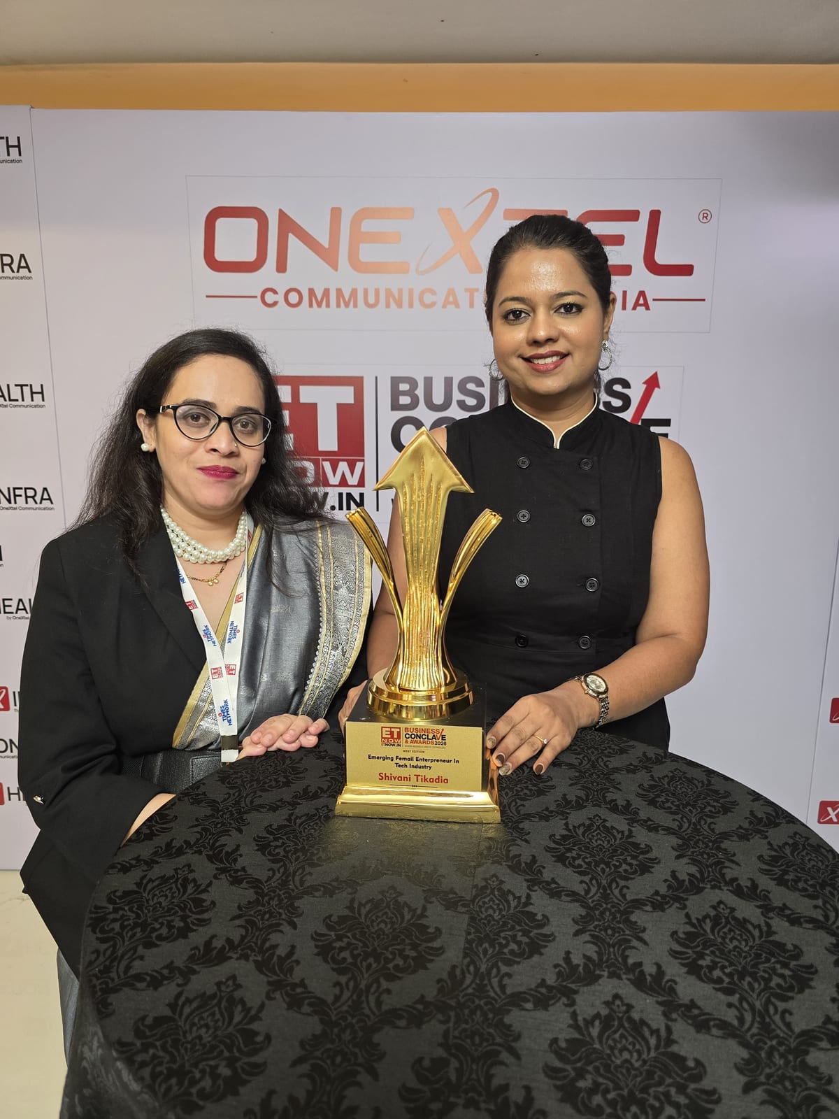 Shivani Tikadia and a SecComply colleague with the Emerging Female Entrepreneur in Tech Industry trophy at the partner wall