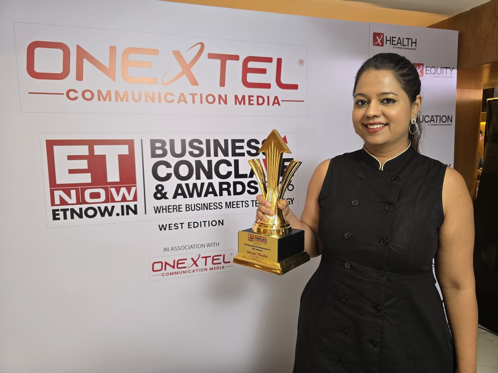 Shivani Tikadia holding a trophy in front of the ETNOW.in Business Conclave and Awards 2026 media wall